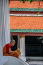 Young Buddhist monk resting on the stairs of Grand Palace temple. Ancient architecture of Asia. Sights of Bangkok.