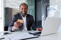 Bank employee, smiling young African American man sitting in office at desk with laptop, holding and showing credit card Royalty Free Stock Photo