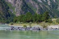 The bank of the Katun river with water containing turquoise clay and a sandy beach, rocky coast against the backdrop of mountains Royalty Free Stock Photo