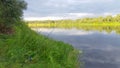 On the bank of the river, overgrown with grass and bushes, there are feeder rods for catching bream on fishing stand. There is a f