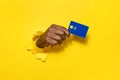 Banking services. African american male hand holding plastic credit card through the torn yellow studio background