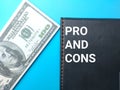 Banknote and notebook with word PRO AND CONS on a blue background Royalty Free Stock Photo