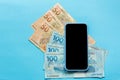 Banknotes of brazilian currency: Reais. Blank smartphone screen and cash bills on colorful bright table