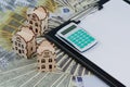 Banknotes dollars and euros are spread out on the table on top of there are small wooden houses