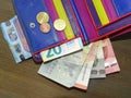 Banknotes and three euro coins in a colorful leather wallet on a table