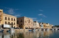 The banks of the Mazaro River in Mazara del Vallo, Italy. The houses are reflected in the water. In the background the blue sky