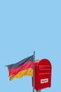 Banner with big red modern metal postbox with note written in German Wahl meaning Vote and standing behind German national flag at