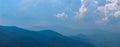 Banner of blue silhouettes of mountains in the distance, with clouds in the blue sky. Mountains and hills in the distance