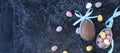 banner with chocolate egg with blue bunny ear bows and multicolored chocolate eggs on a black textured background. Royalty Free Stock Photo