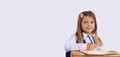 Banner. A cute caucasian schoolgirl, sitting at her desk smiling, looking to camera is studying a new topic. Gray