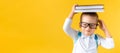 Banner Funny Preschool Child Boy in Glasses with Book on Head and Bag on Yellow Background Copy Space. Happy smiling kid Royalty Free Stock Photo