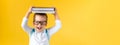 Banner Funny Preschool Child Boy in Glasses with Book on Head and Bag on Yellow Background Copy Space. Happy smiling kid Royalty Free Stock Photo