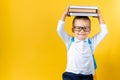 Banner Funny Preschool Child Boy in Glasses with Book on Head and Bag on Yellow Background Copy Space. Happy smiling kid Royalty Free Stock Photo