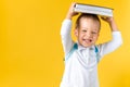 Banner Funny Preschool Child Boy 3-4 years with Book on Head and Bag on Yellow Background Copy Space. Happy Smiling Kid Royalty Free Stock Photo