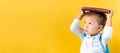 Banner Funny Preschool Child Boy 3-4 years with Book on Head and Bag on Yellow Background Copy Space. Happy Smiling Kid Royalty Free Stock Photo