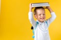 Banner Funny Preschool Child Boy 3-4 years with Book on Head and Bag on Yellow Background Copy Space. Happy Smiling Kid Royalty Free Stock Photo