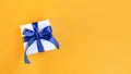 Banner of a Gift wrapped in white paper with a blue bow made of satin on festive yellow orange background Royalty Free Stock Photo