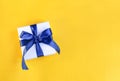 Banner of a Gift wrapped in white paper with a blue bow made of satin on festive yellow orange background Royalty Free Stock Photo