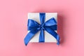 Gift wrapped in white paper with a blue bow made of satin on soft pink background Royalty Free Stock Photo