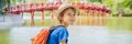 BANNER, LONG FORMAT Caucasian boy tourist on background of Red Bridge in public park garden with trees and reflection in Royalty Free Stock Photo