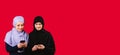 Banner- long format. Pretty muslim women texting using smartphones isolated on red background with smile on smart faces