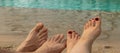 banner with male and female feet lie on the sand against the background of blue water. two pairs of legs. concept of Royalty Free Stock Photo