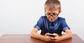 Banner Portrait of smiling boy with glasses using mobile phone on school Desk on white background Modern mobile and communications