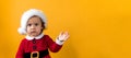 Banner Serious Portraite Cute Fun Cheerful Chubby Baby Girl in Santa Hat Waving Hand At Yellow Background. Child Play Royalty Free Stock Photo