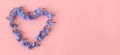 Banner: small blue flowers laid out in the shape of a heart on a pink background, top view, space for text