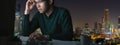 Banner of young asian man sitting on desk table work late and hard with computer laptop at office with night light city view Royalty Free Stock Photo