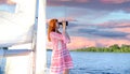 A young girl in a pink mini dress standing on a yacht and looking to the right through binoculars Royalty Free Stock Photo