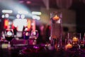 Banquet table decorated with burning candles in glass vases in restaurant hall. In the background party with silhouettes Royalty Free Stock Photo