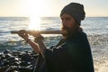 Bansuri player playing music in sunshine at sea shore.