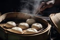 bao bun being carefully separated from its bamboo steamers, with hint of steam still visible