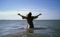 Baptism. Young woman in a long dress standing in the water with her hands raised