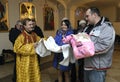 Baptizing for baby. Man and woman standing with a baby on hands and priest cutting off a patch of hairs from head of child