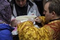 Baptizing for baby. Man and woman standing with a baby on hands and priest cutting off a patch of hairs from head of child