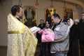 Baptizing for baby in rural church. Priest standing in front of woman and man with a baby on hands and reading Bible