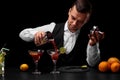 An attractive bartender pours a cocktail in a margarita glass, oranges, lemon, slices of lime on a black background. Royalty Free Stock Photo