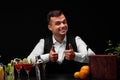 A bartender shows big thumbs up, a bar counter with oranges, lemon, a shaker, margarita glasses on black background. Royalty Free Stock Photo