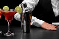 A shaker on a bar counter, a margarita glass full of cocktail, a hand of a bartender on a black blurred background. Royalty Free Stock Photo