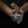 A bar of soap jumps out of a woman`s foam-filled hands on a dark background Royalty Free Stock Photo