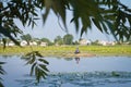 Old unknown fisherman in a wooden punt boat fishing with rods, reflections on still surface of Riv river