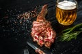 Barbecue dry aged rib of beef with spice, vegetables and a glass of light beer close-up on black wooden background Royalty Free Stock Photo