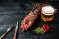 Barbecue dry aged rib of beef with spice, vegetables and a glass of light beer close-up on black wooden background Royalty Free Stock Photo