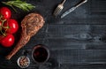 Barbecue dry aged rib of beef with spice, vegetables and glass of red wine close-up on black wooden background Royalty Free Stock Photo