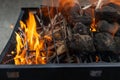 Barbecue grill with burning charcoal and wood - black rectangular grill - orange and yellow flames - blurred concrete background