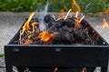 Barbecue grill with burning charcoal and wood - black rectangular grill - orange and yellow flames - blurred concrete background