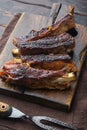 Barbecue pork spare ribs, on wooden serving board, with barbeque knife and meat fork, on old dark wooden table background