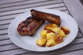 Barbecued Sticky Ribs and pork chops from grill with oven baked potatoes on a plate with wooden background Royalty Free Stock Photo